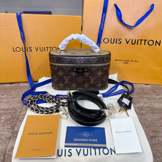 Louis Vuitton monogram cosmetic bag displayed with its chain strap, black shoulder strap, box, dust bag, branded store card, booklet, and shopping bags on a beige surface.